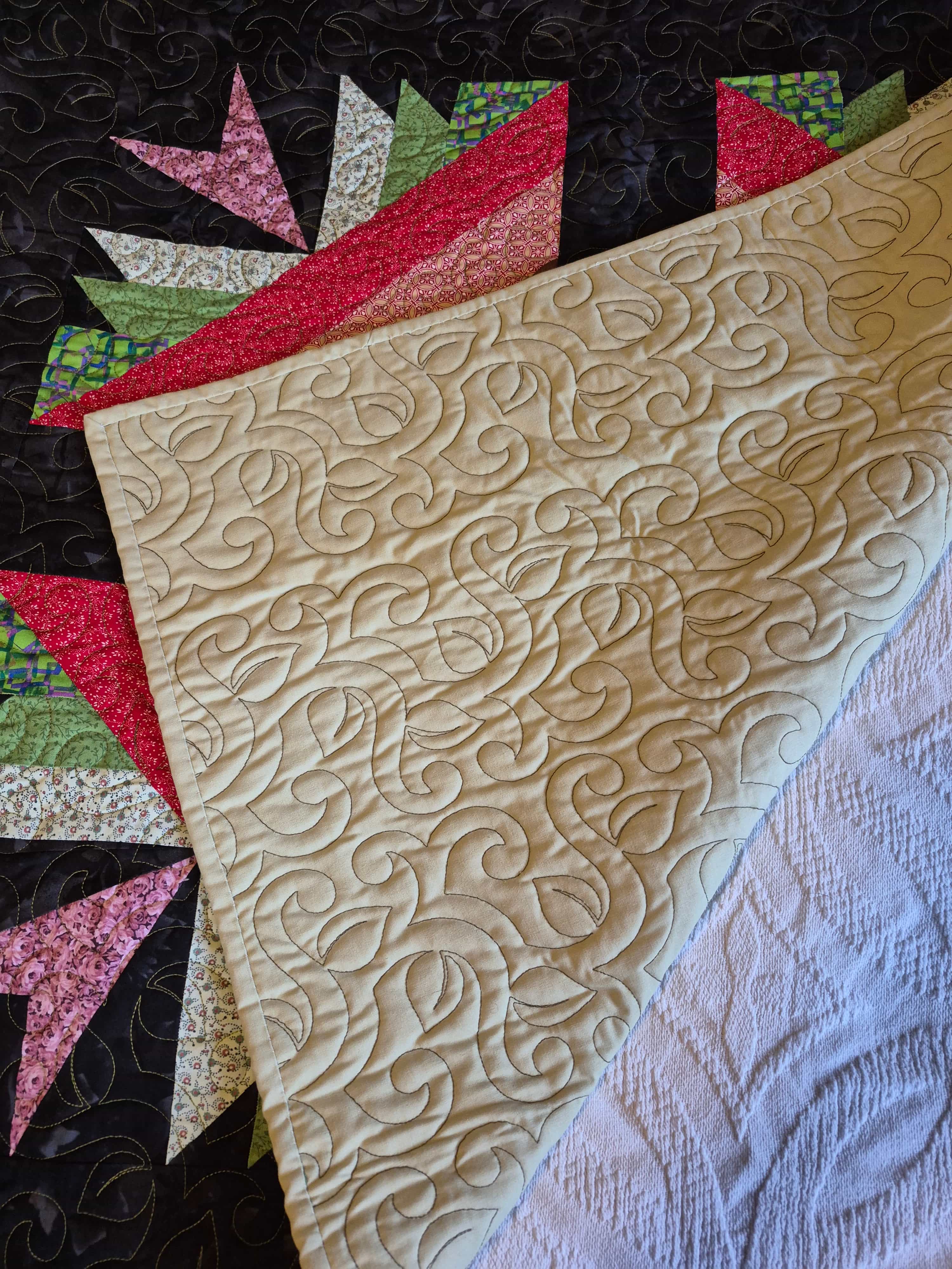 Autumn leaves quilt folded to show elegant scroll quilting on cream backing