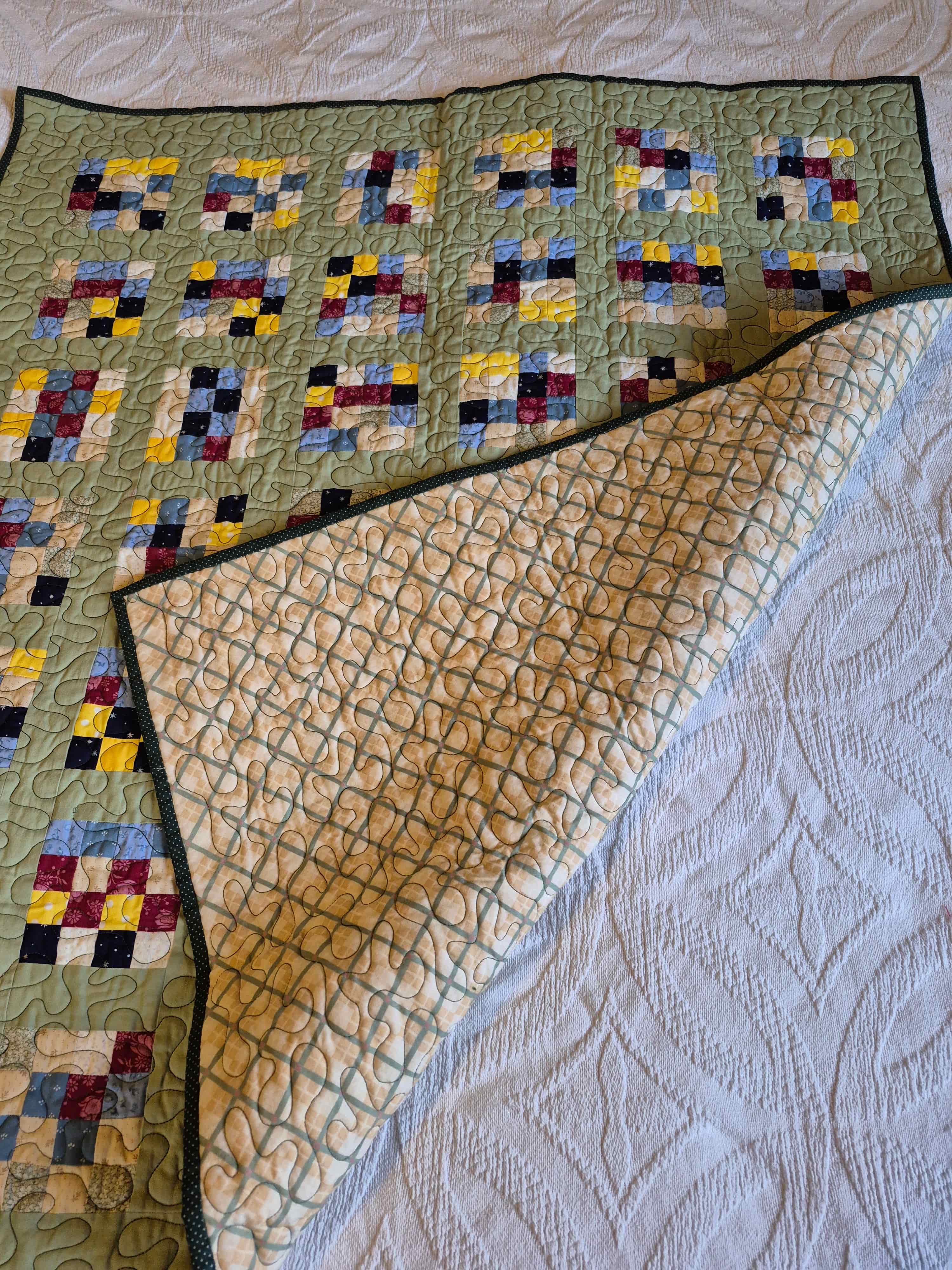 Sage green patchwork quilt folded to show geometric quilting on tan backing