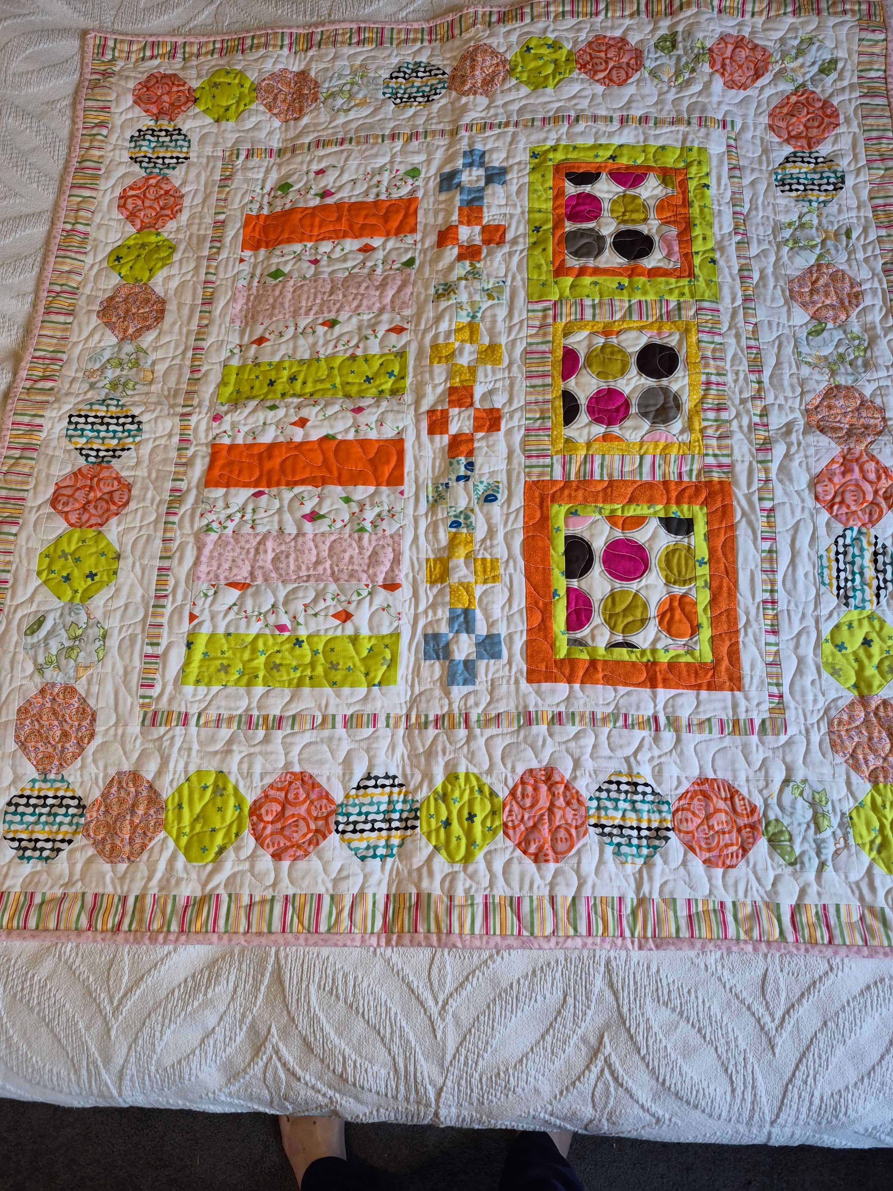 Modern baby quilt with hexagon border and colorful strip blocks in orange, green, and pink